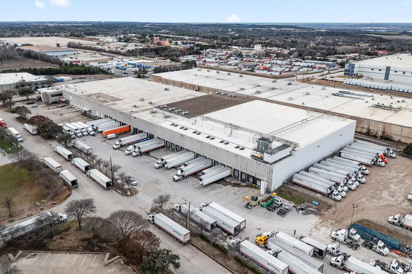 Aerial view of large industrial warehouse facility with loading docks and trucks in sprawling commercial park.